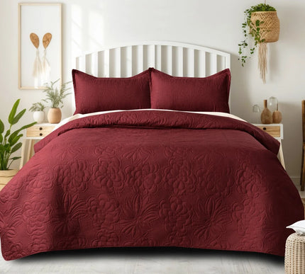 Burgundy quilt set on a bed in a bedroom with plants and decor.