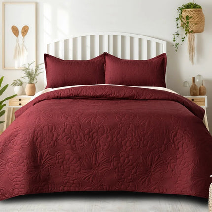 Burgundy quilt set on a bed in a bedroom with plants and decor.