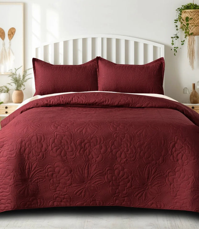 Burgundy quilt set on a bed in a bedroom with plants and decor.