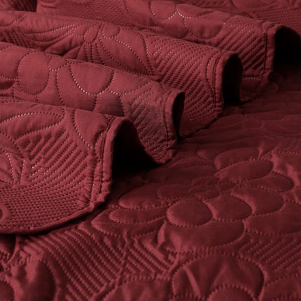 Close-up of a textured burgundy quilt with leaf patterns