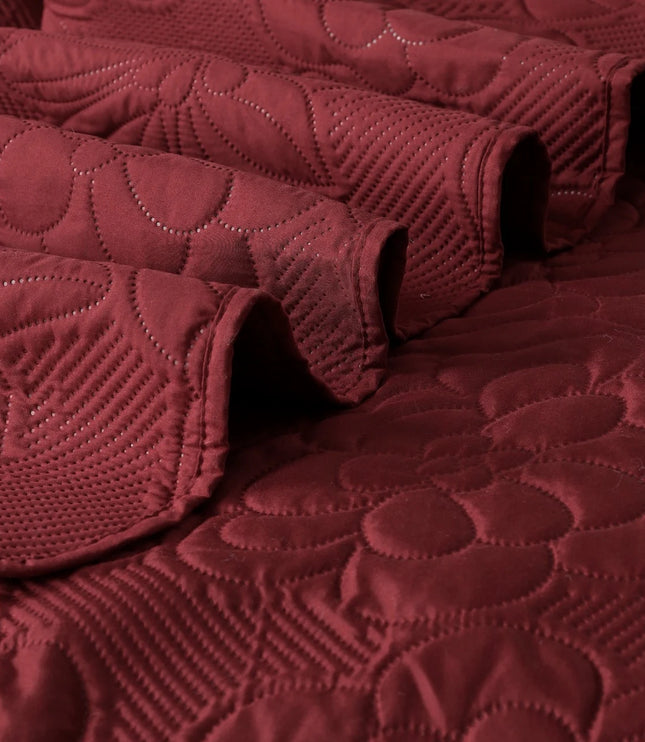 Close-up of a textured burgundy quilt with leaf patterns