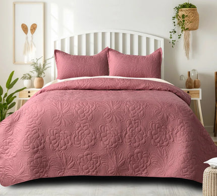 Pink floral quilt set on a bed in a bedroom with plants and decor.