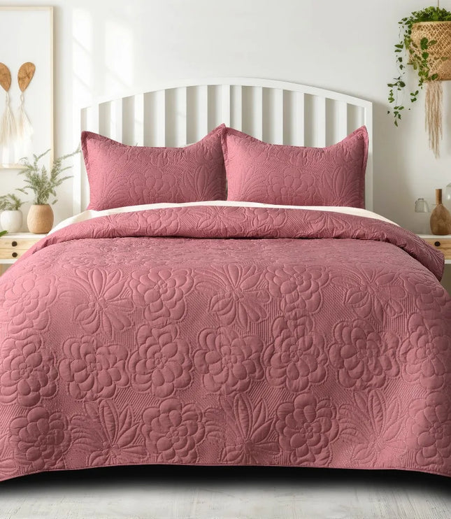 Pink floral quilt set on a bed in a bedroom with plants and decor.