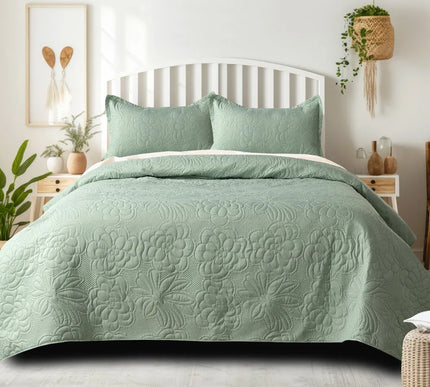 Green quilted bedspread on a bed in a well-lit bedroom with plants and decor.
