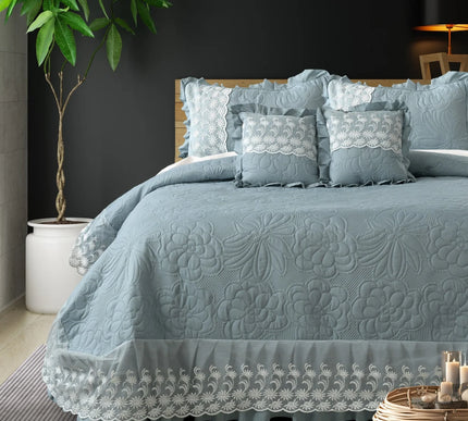 Blue textured bedspread with lace details on a bed in a bedroom setting.