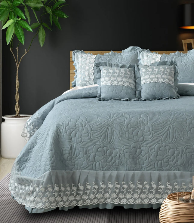 Blue textured bedspread with lace details on a bed in a bedroom setting.