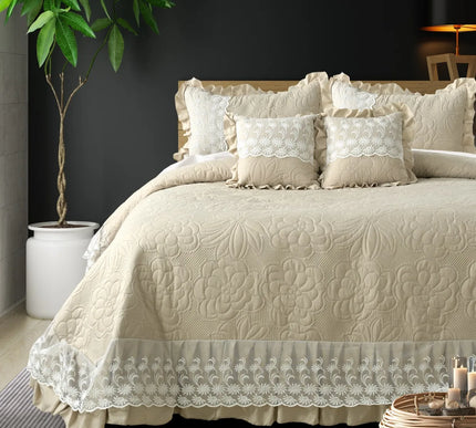 Beige quilted bedspread with lace details on a bed in a bedroom setting.