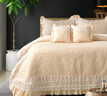 Beige quilted bedspread with lace trim on a bed in a bedroom setting.