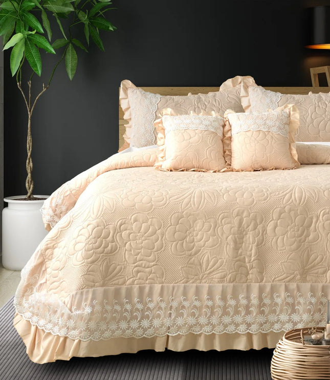 Beige quilted bedspread with lace trim on a bed in a bedroom setting.