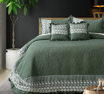 Green quilted bedspread with lace details on a bed in a bedroom setting.