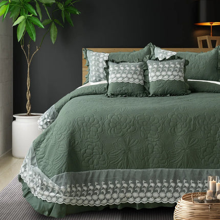 Green quilted bedspread with lace details on a bed in a bedroom setting.