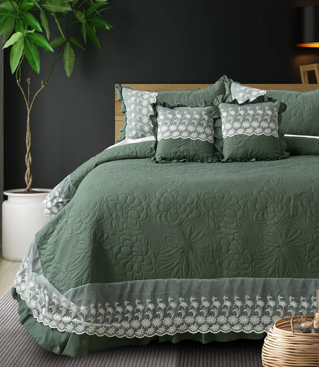 Green quilted bedspread with lace details on a bed in a bedroom setting.