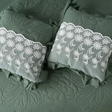Two green pillows with white lace embroidery on a textured green fabric background