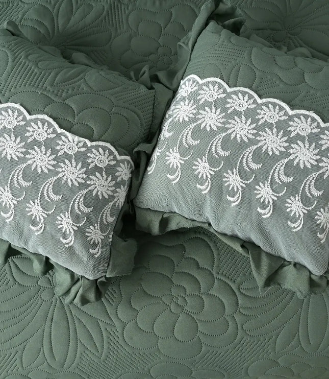 Two green pillows with white lace embroidery on a textured green fabric background