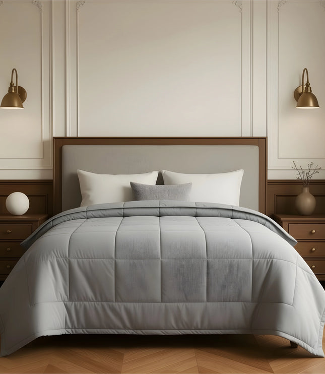 Gray comforter on a bed in a bedroom setting with wooden furniture and wall sconces.