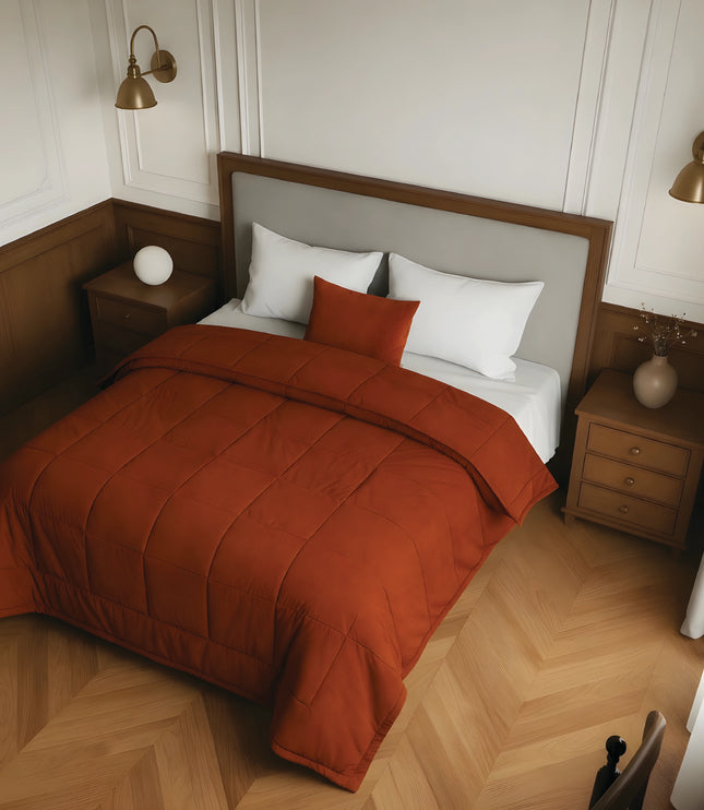 Bedroom with a bed featuring a rust comforter and white pillows, wooden nightstands, and wall lamps.