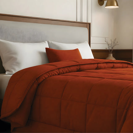Bed with rust comforter and white pillows in a bedroom setting