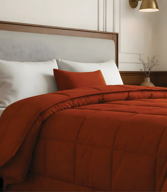 Bed with rust comforter and white pillows in a bedroom setting