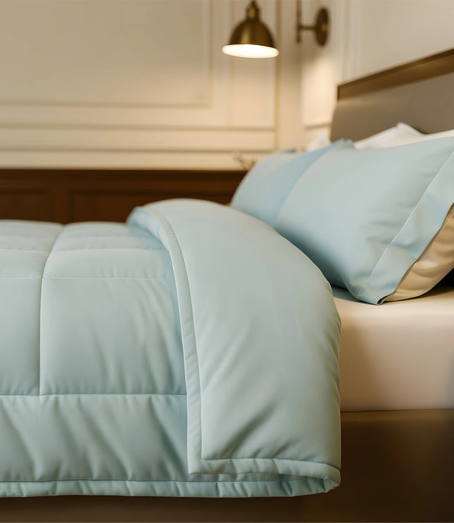 Bed with light blue comforter and pillows in a bedroom setting