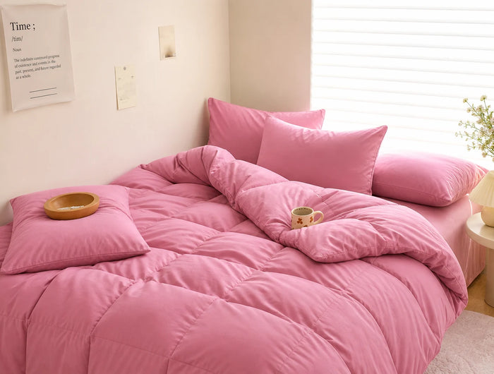 Pink bedspread and pillows on a bed in a well-lit room.