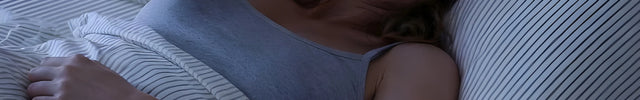 Woman lying in bed at night with a soft glow from a lamp.